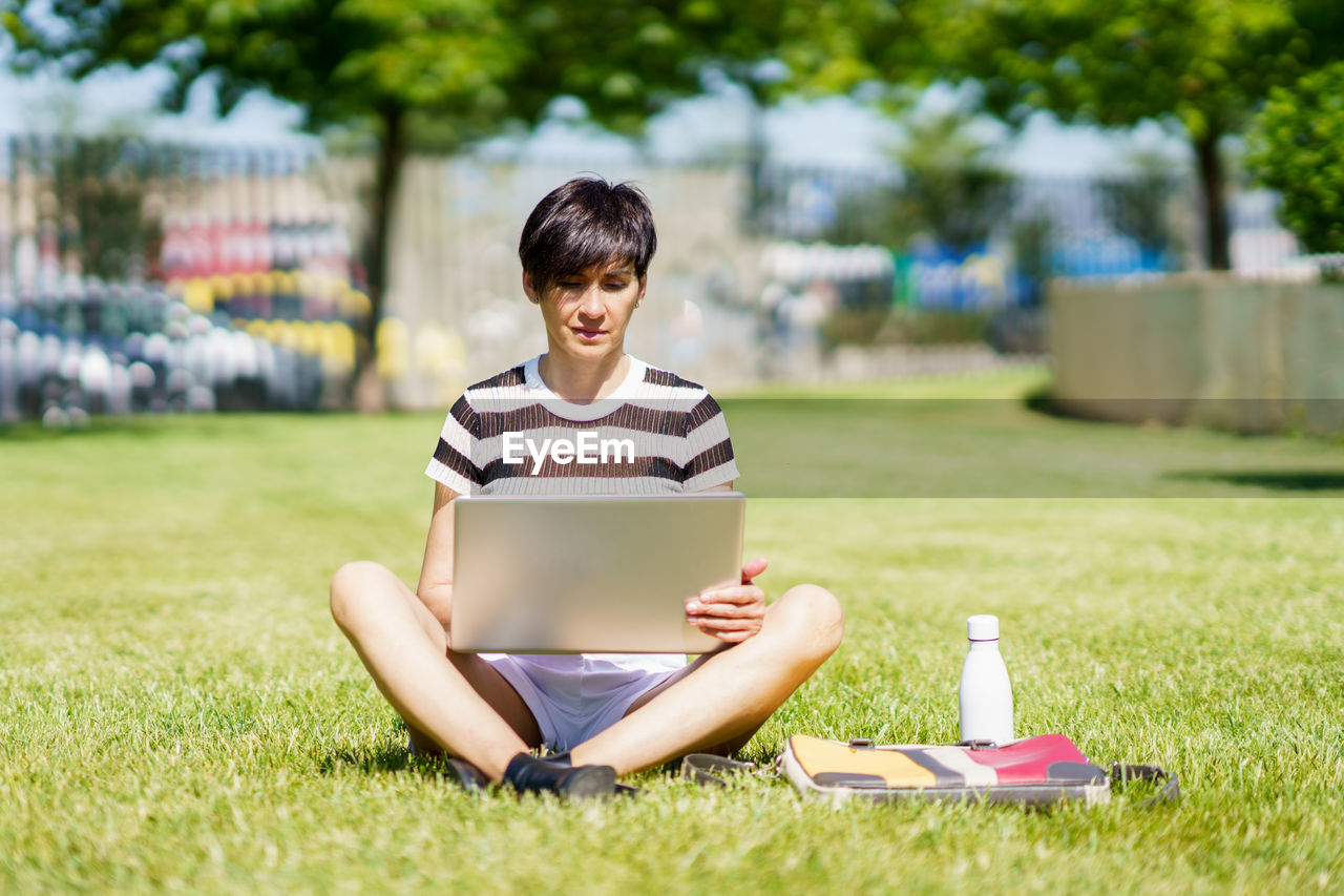 young woman using laptop while sitting on field in park