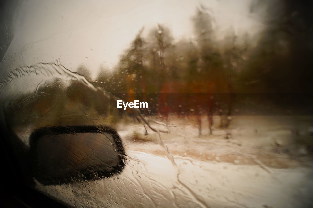 Side-view mirror seen through wet car window during rainy season