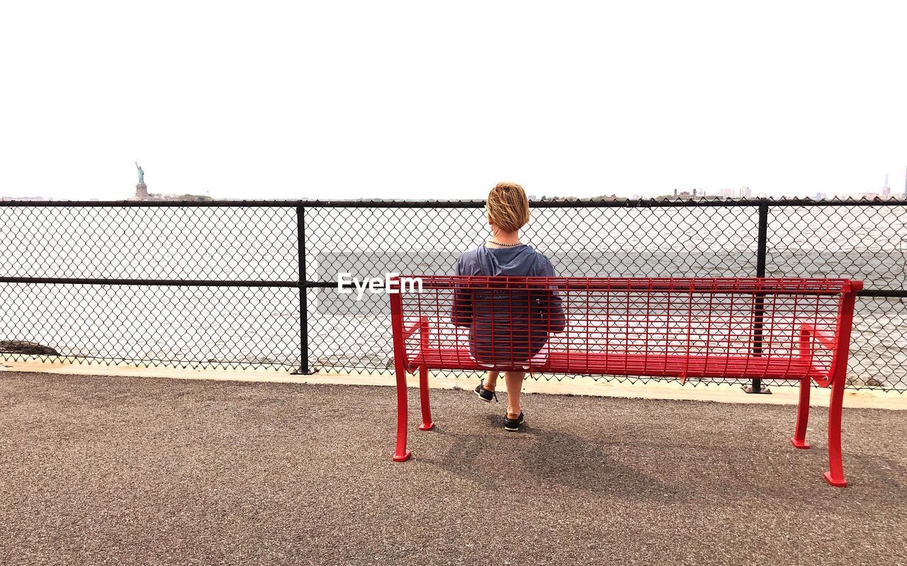 Rear view of woman looking at river while sitting on bench 