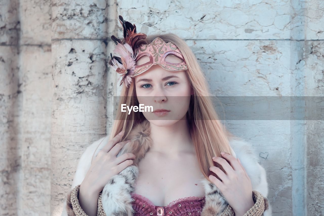 Portrait of young woman with eye mask standing against wall