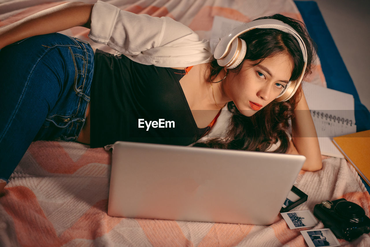Portrait of young woman wearing headphone lying on bed at home
