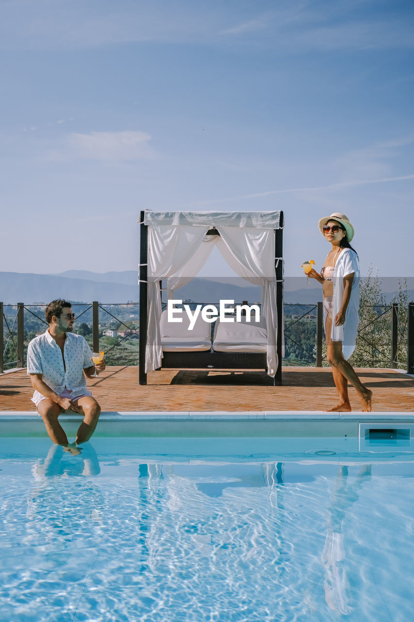 Full length of couple by swimming pool against sky