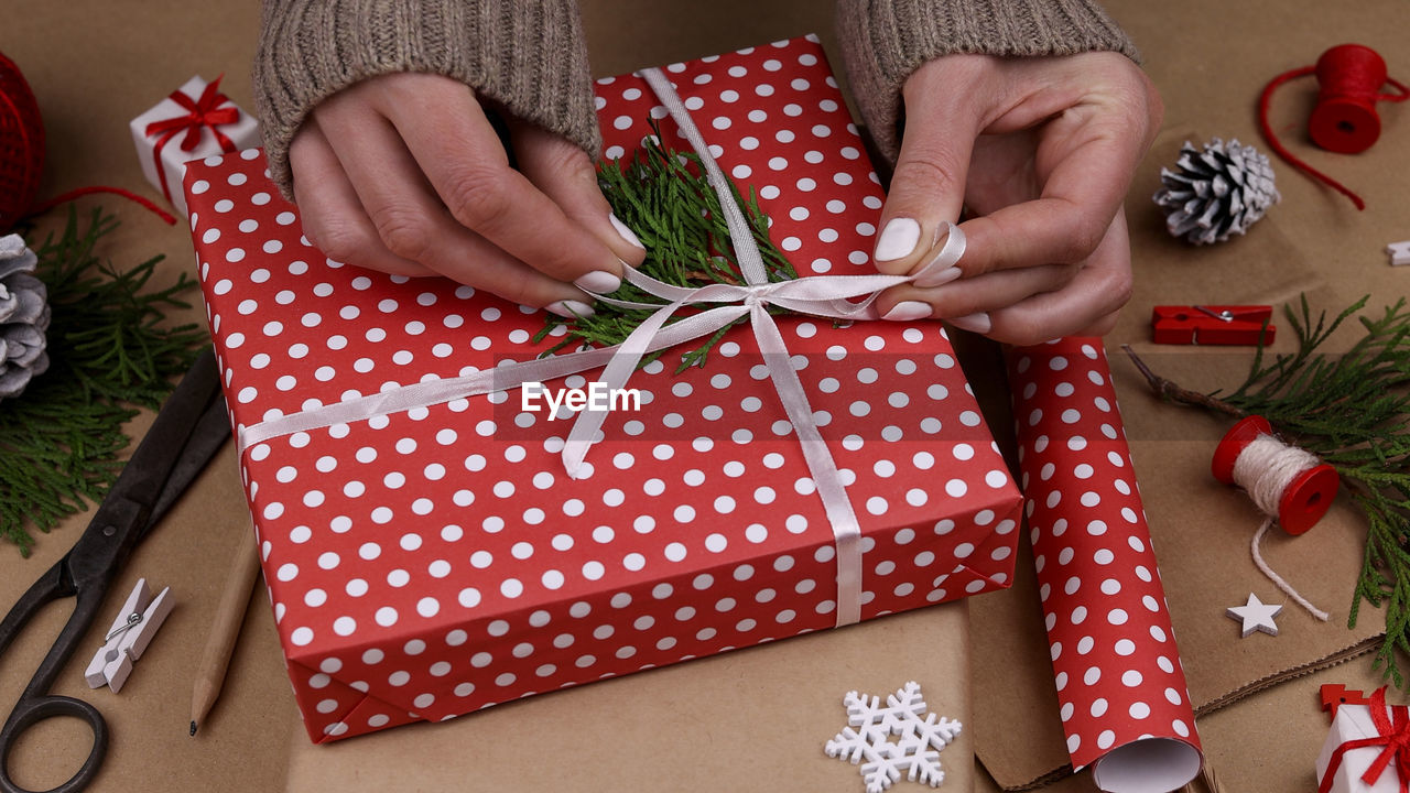 Close up woman hands packing and wrapping christmas gift boxes with red paper, high angle view