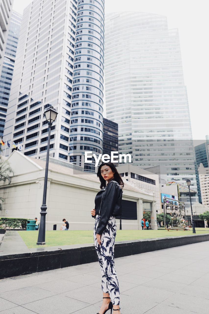 Low angle portrait of young woman standing against modern buildings in city