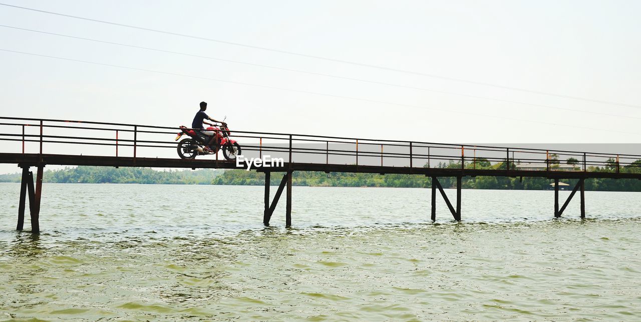 Low angle view of man riding motorcycle on bridge over river