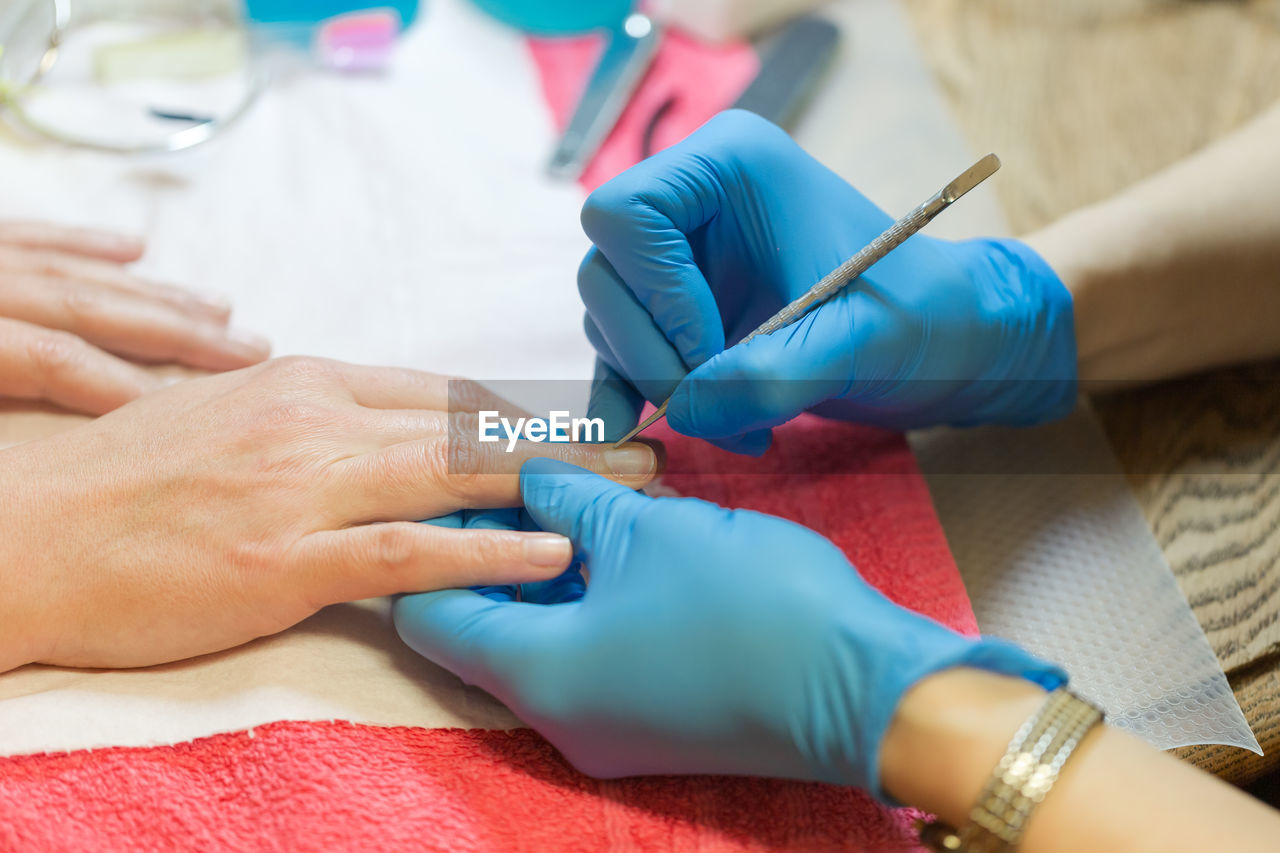 Self emplyed woman with blue sintetic gloves making manicure. close up focus on hands.