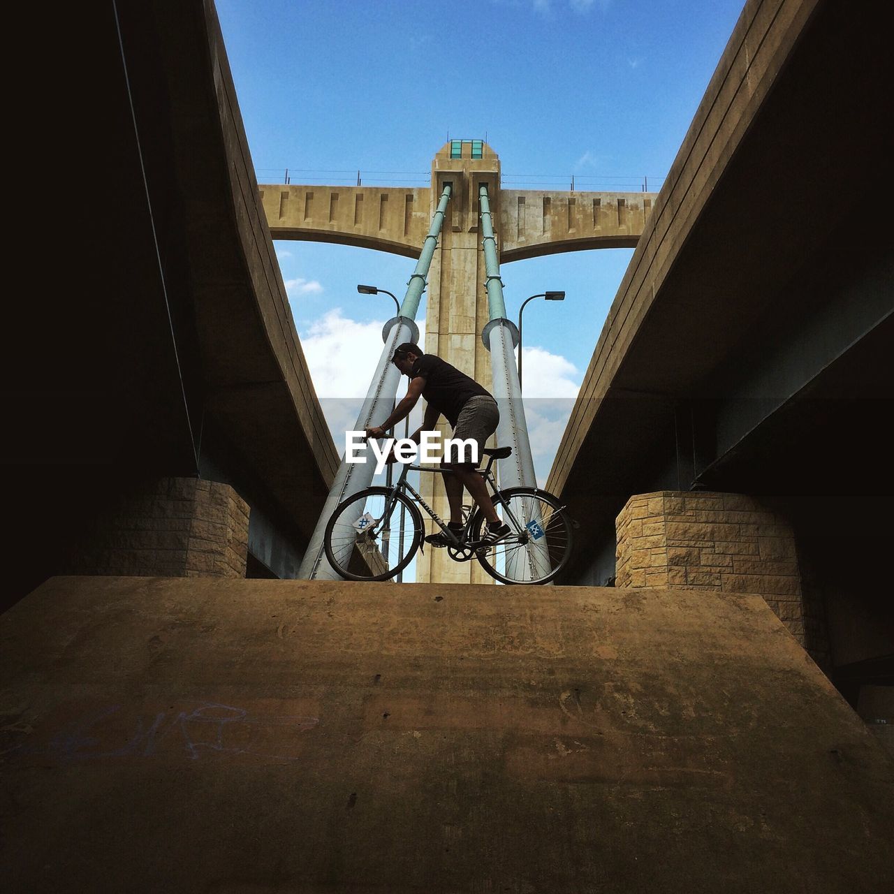 Low angle view of man balancing on bicycle along bridge
