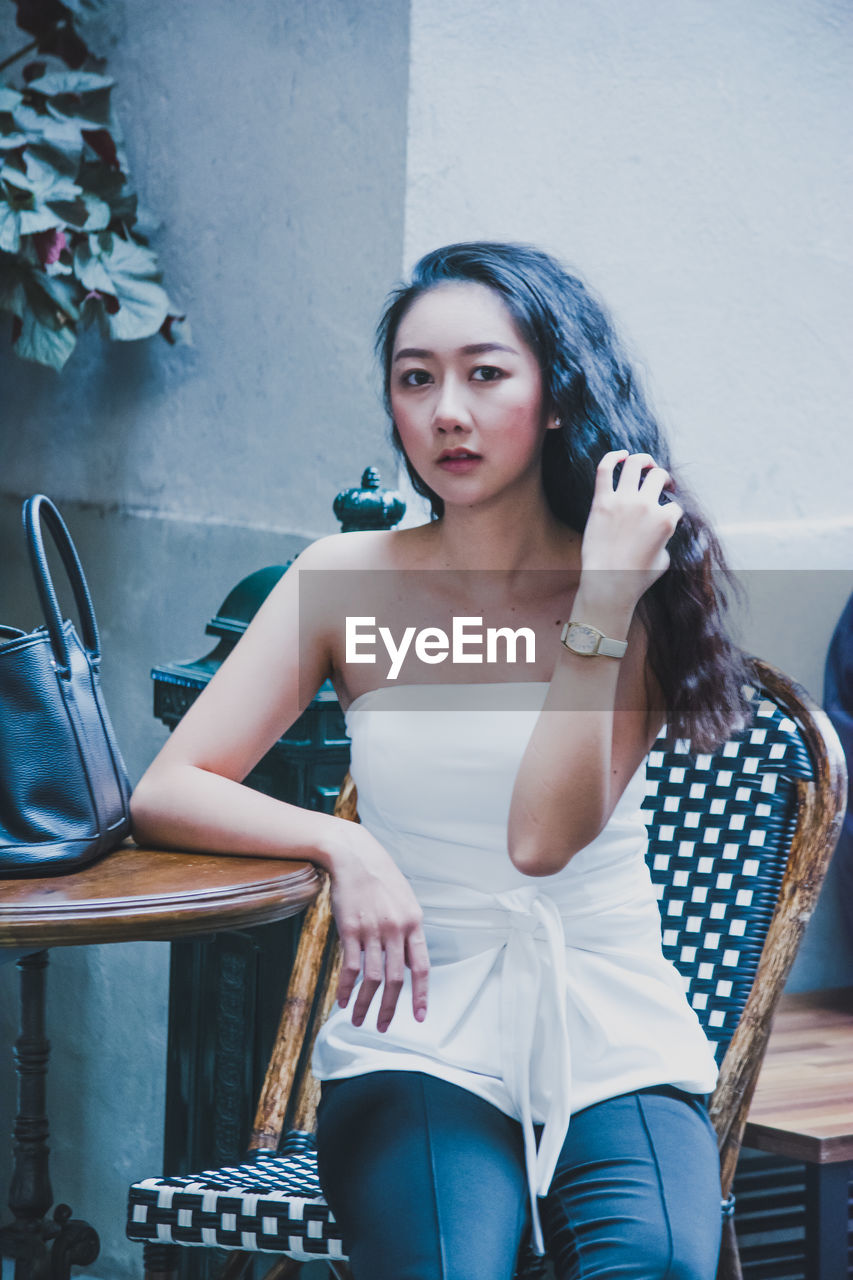 Portrait of young woman sitting at sidewalk cafe in city