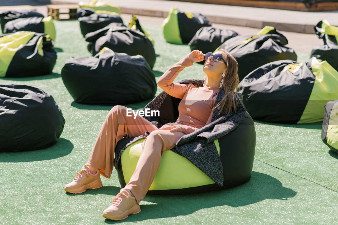 Pretty white young woman is lying on an easy chair in the open air wearing sunglasses and smiling