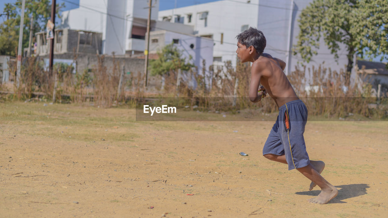 Full length side view of shirtless boy playing on field during sunny day