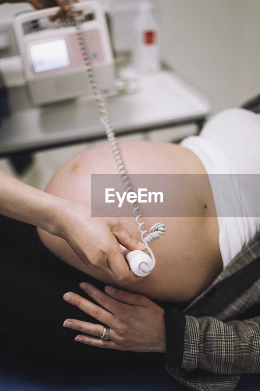 Hands of female gynecologist doing ultrasound of patient's pregnant belly in medical clinic