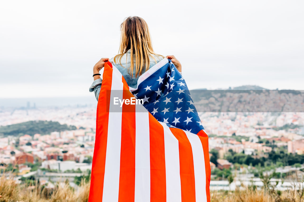 Rear view of woman with american flag standing against the sky