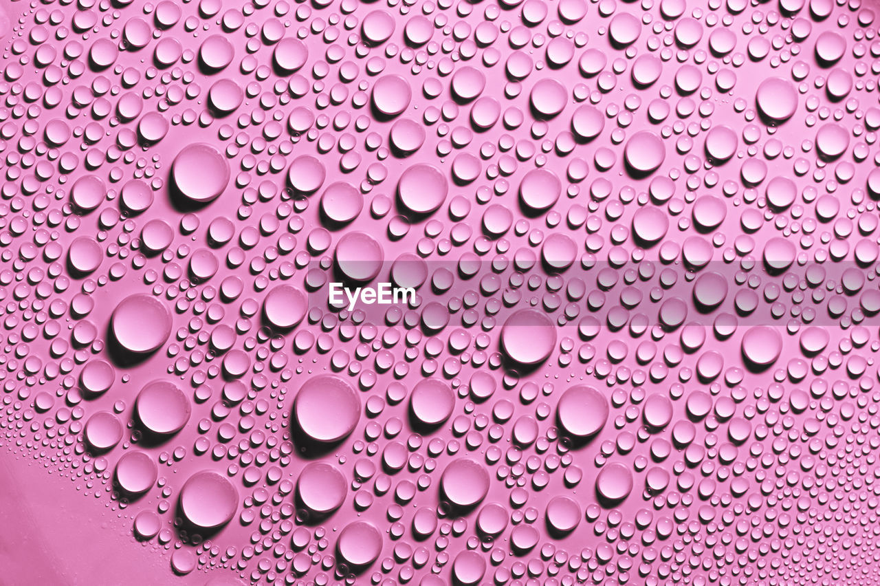 Detail and close up of condensation drops of pink water on surface. texture background decoration.