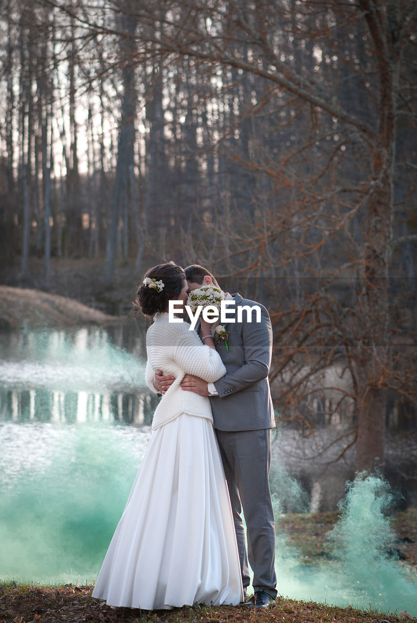 Newlywed couple kissing while standing against lake