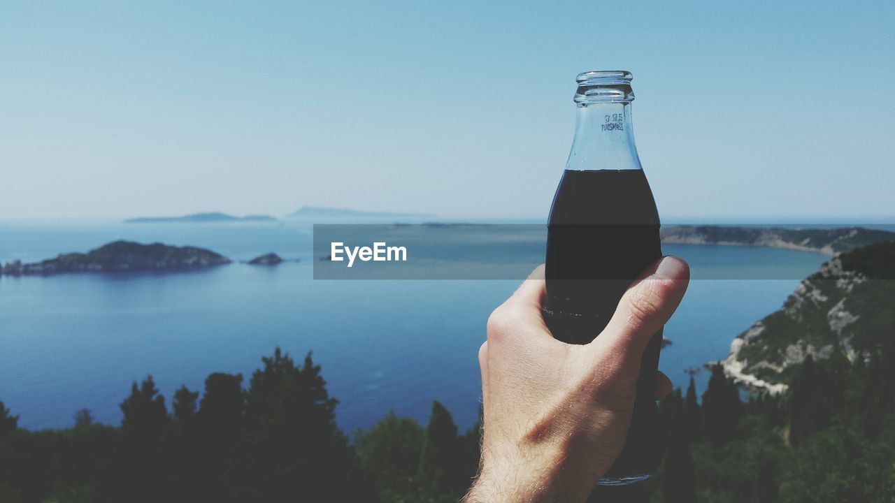 Cropped image of person holding drink against lake