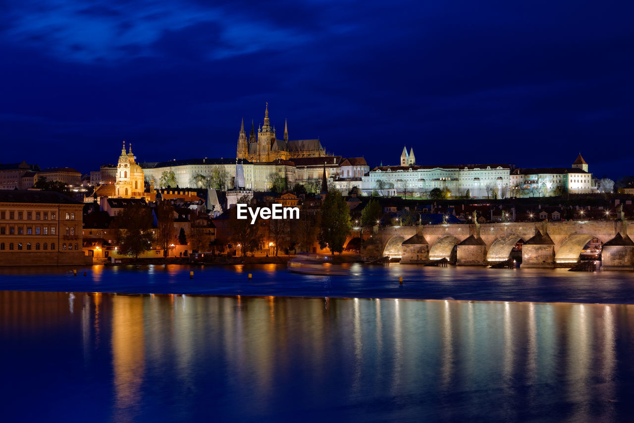 Illuminated buildings by river in city