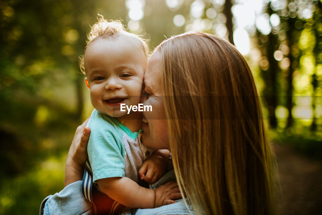 Happy mom snuggling baby boy outside in forest