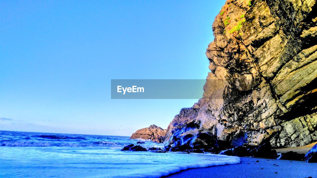 Rock formation in sea against clear blue sky