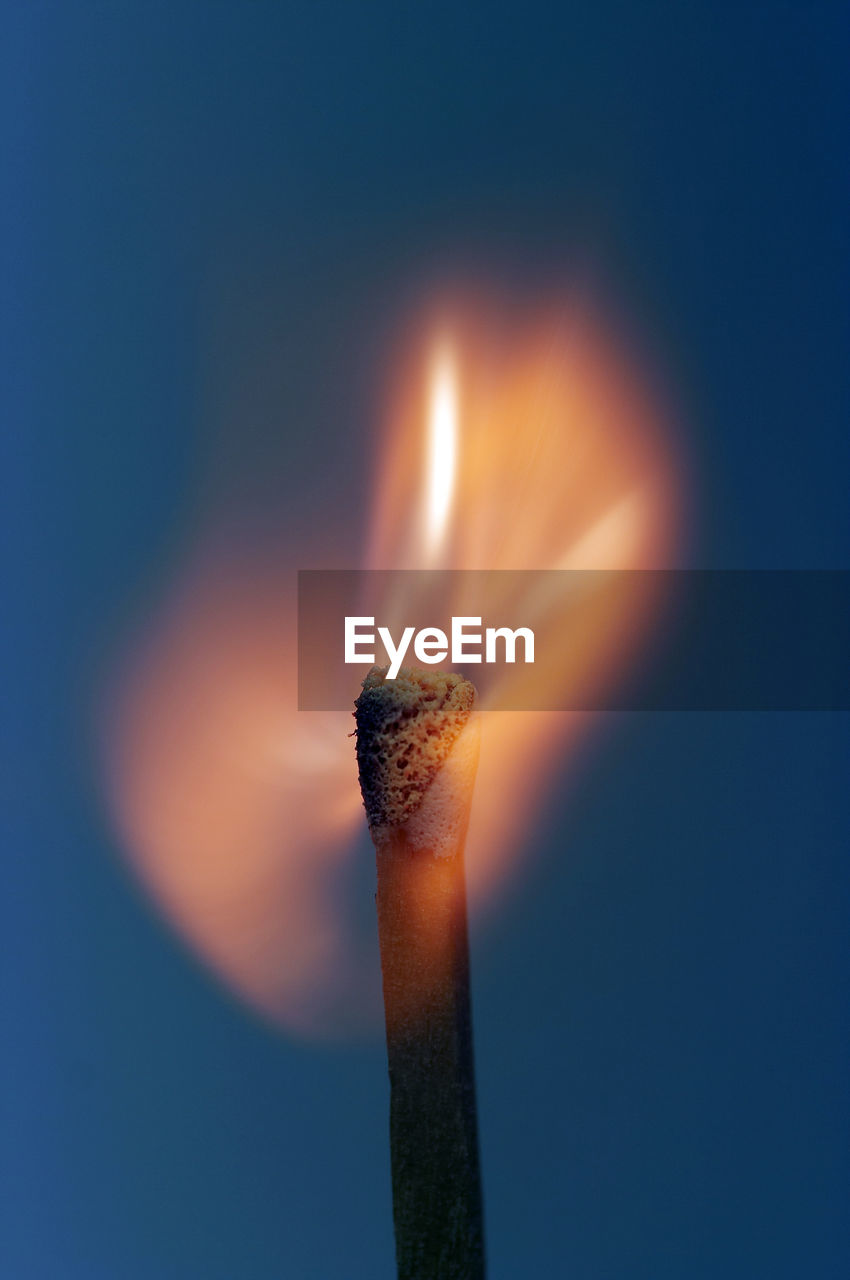 Close-up of burning matchstick over blue background