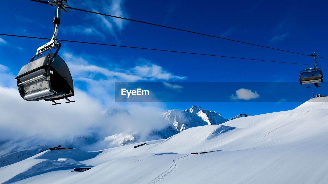 Low angle view of ski lifts over snow covered mountain against sky