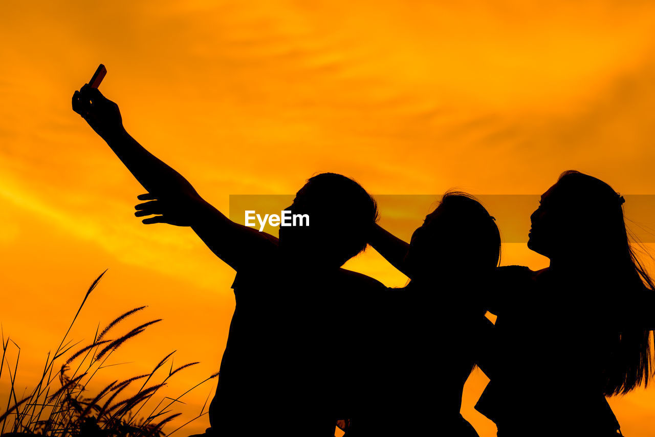 Silhouette friends taking selfie against orange sky