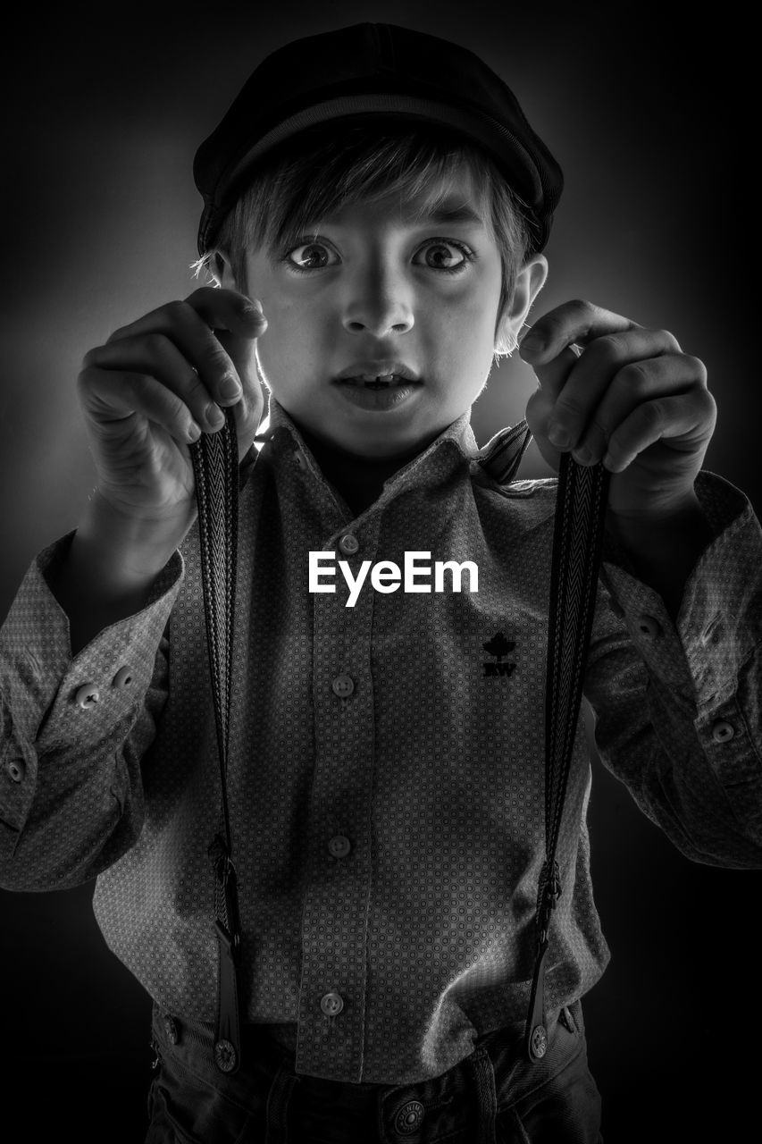 Portrait of boy wearing suspenders while standing against black background