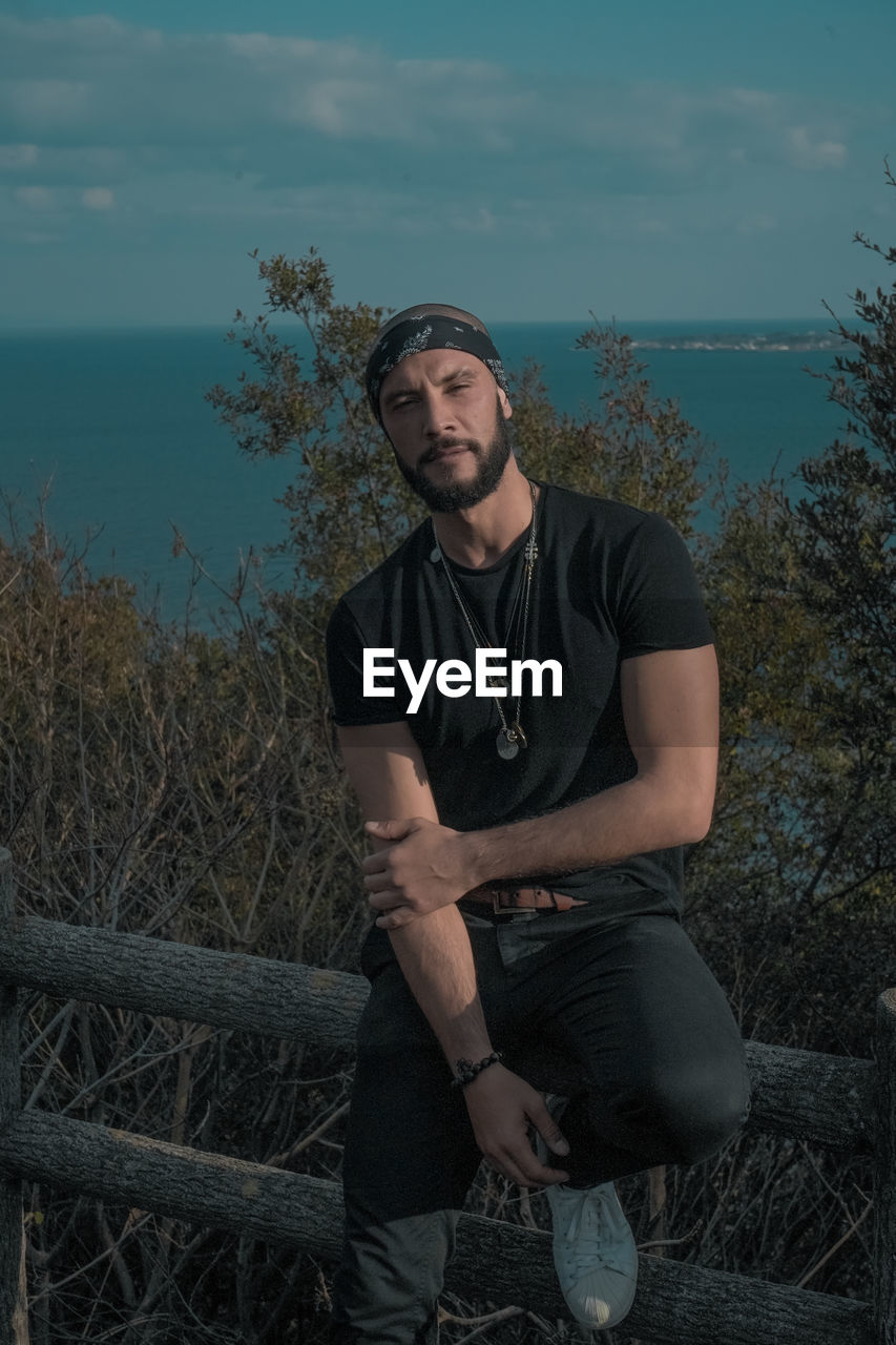 Portrait of fashionable man sitting against sea