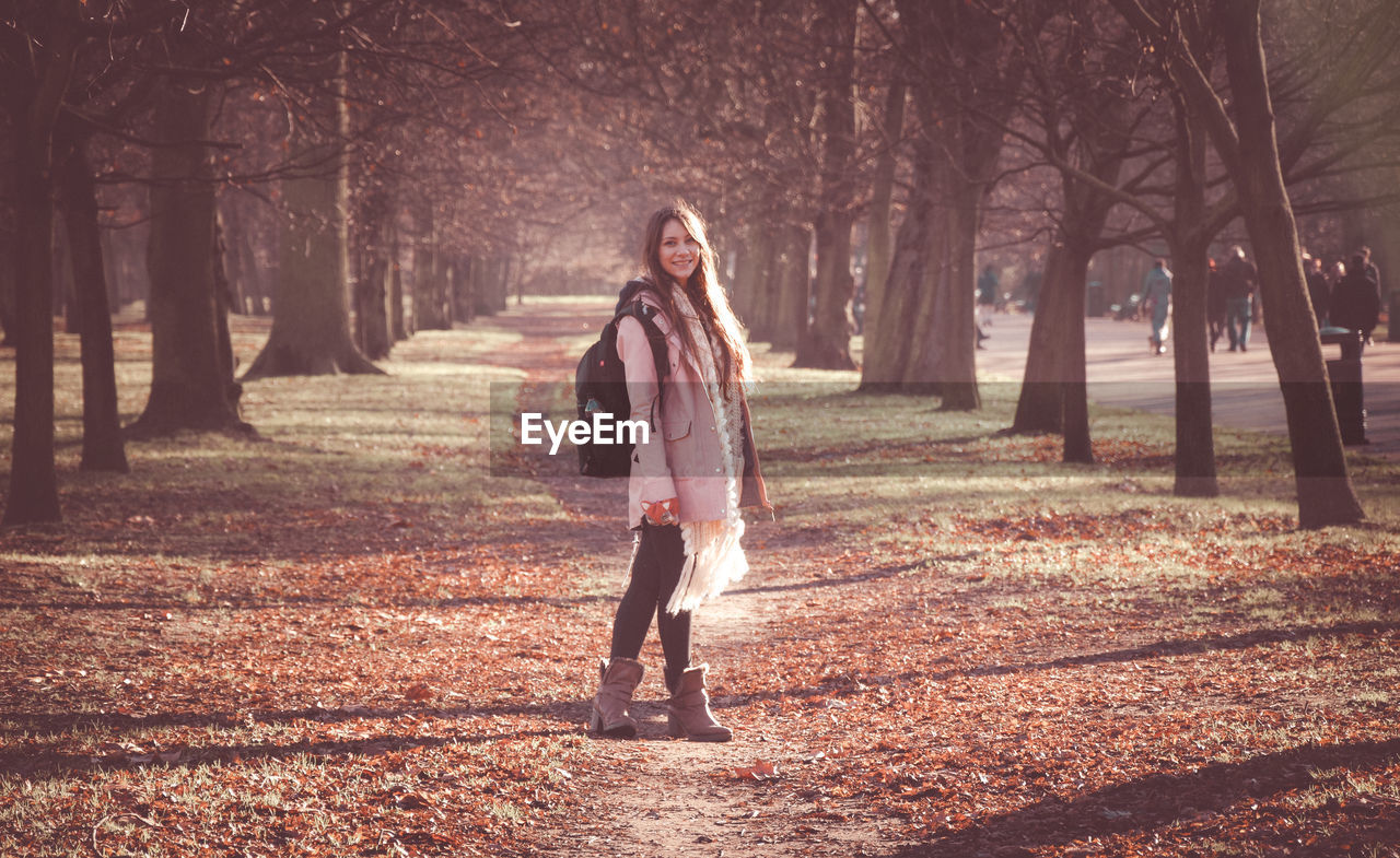 FULL LENGTH OF WOMAN STANDING BY TREE TRUNK