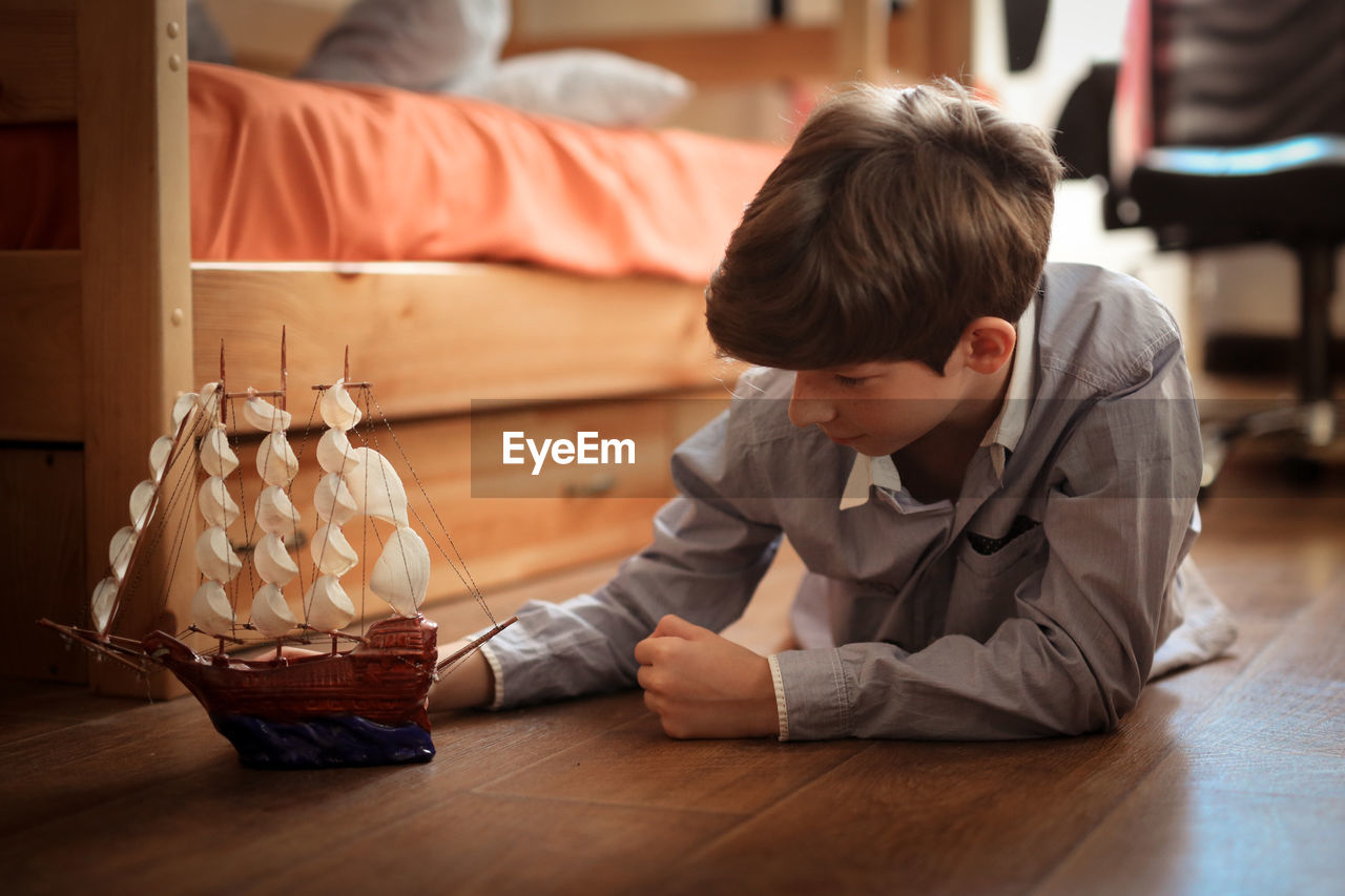 Boy teen plays with ship model on the floor in real children's room