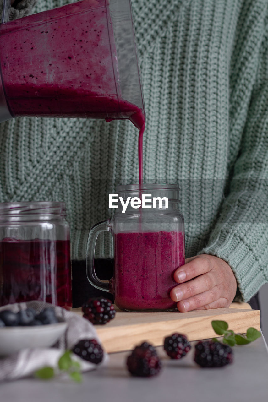 Crop person filling from blender glass jar with yummy vitamin smoothie of sweet fresh berries and mint after preparing breakfast at home