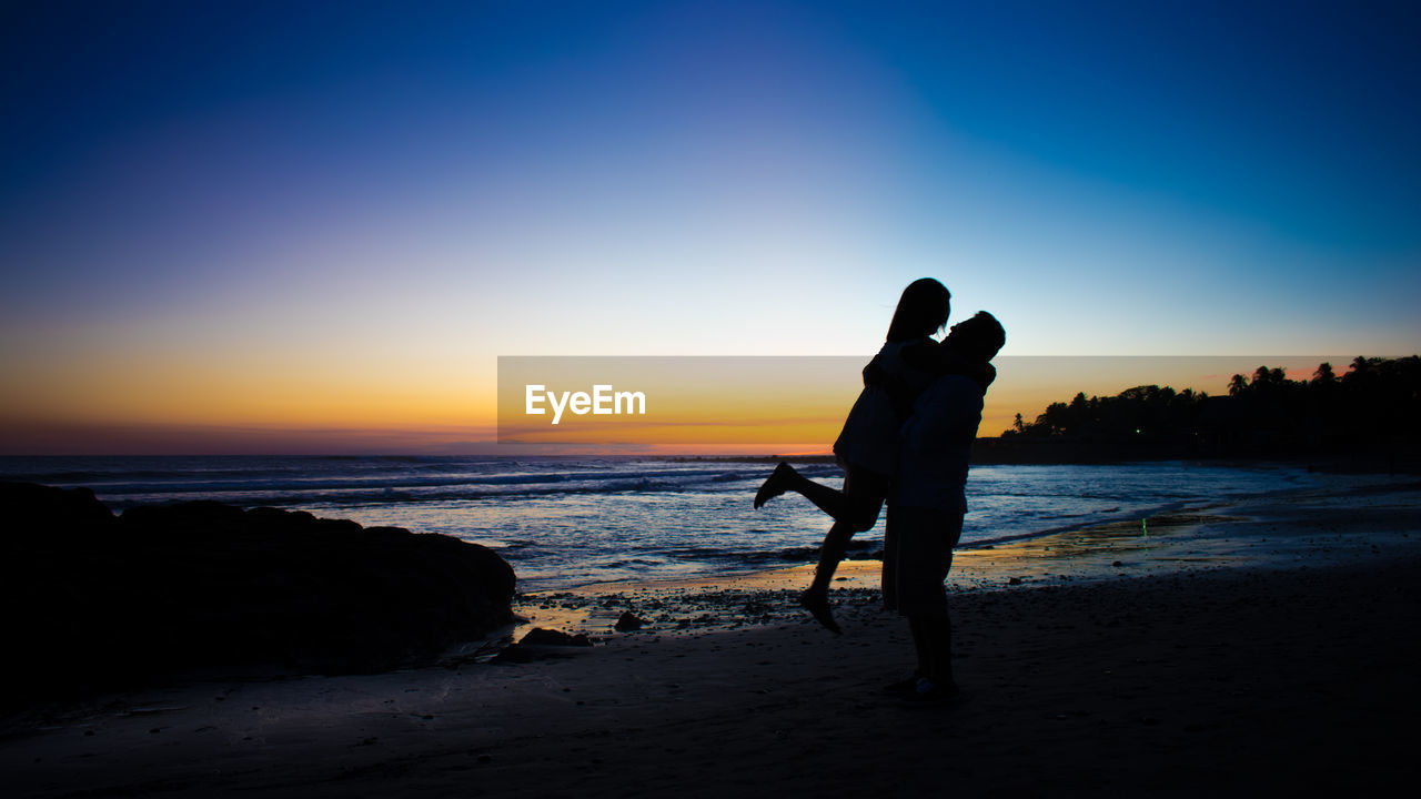Silhouette couple embracing at beach against sky during sunset