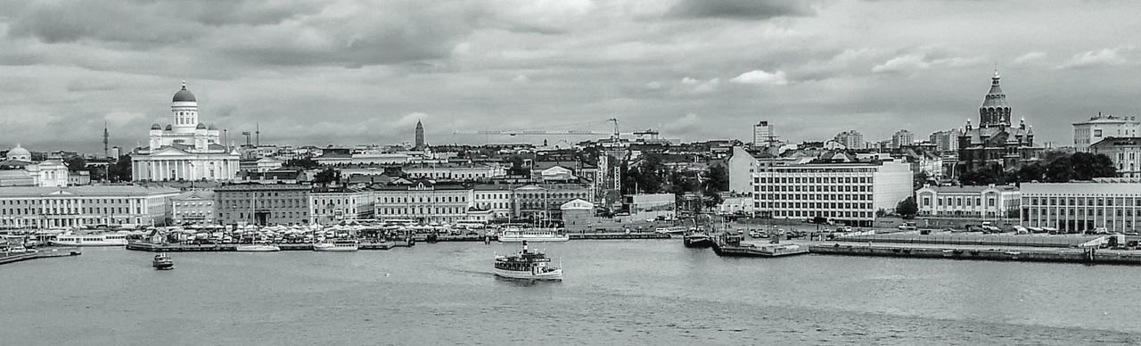 Boats in river against buildings against cloudy sky