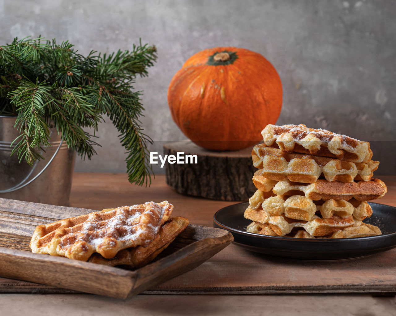 Homemade waffles with sugar bubble and orange pumpkin on a wooden tray