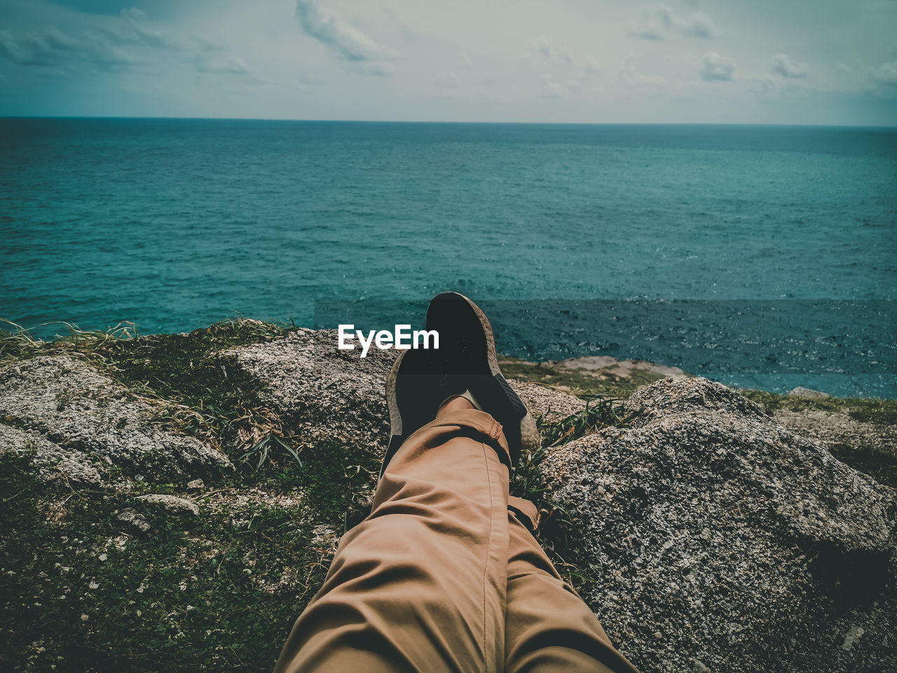 Low section of man relaxing on rock formation by sea