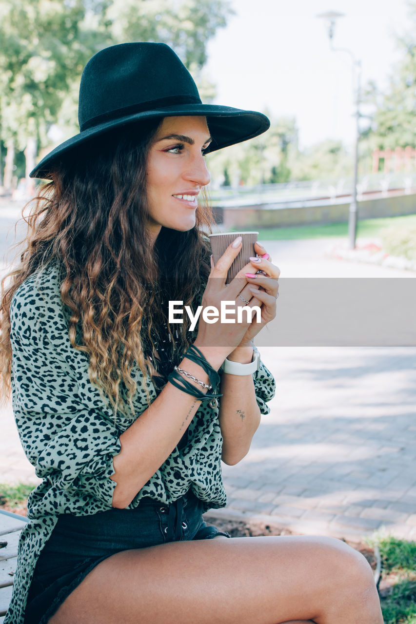 Portrait of beautiful stylish young woman wearing black felt hat drinking coffee. .