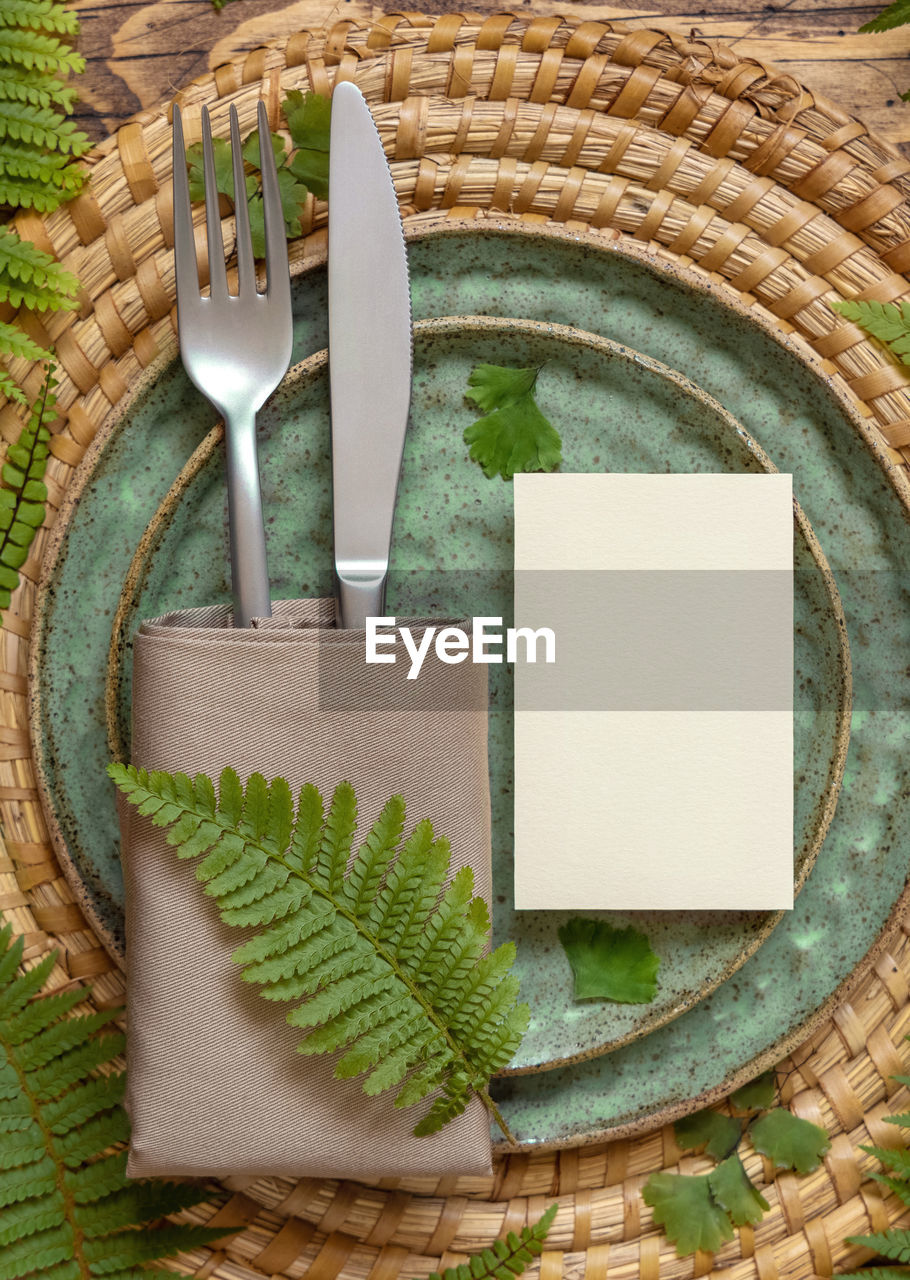 Blank paper card on table setting decorated with fern leaves on wooden table top view