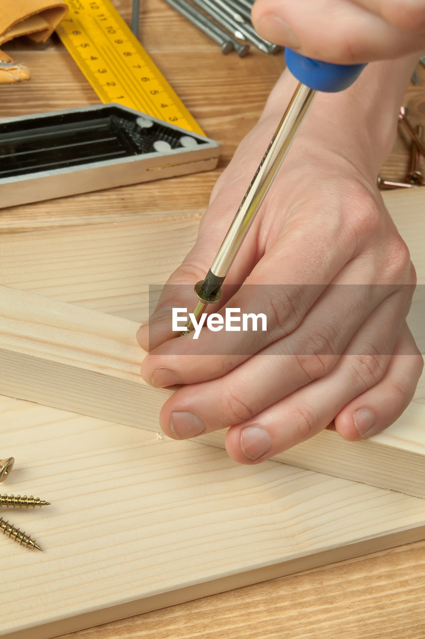 Close-up of craftsperson using screwdriver on wooden plank