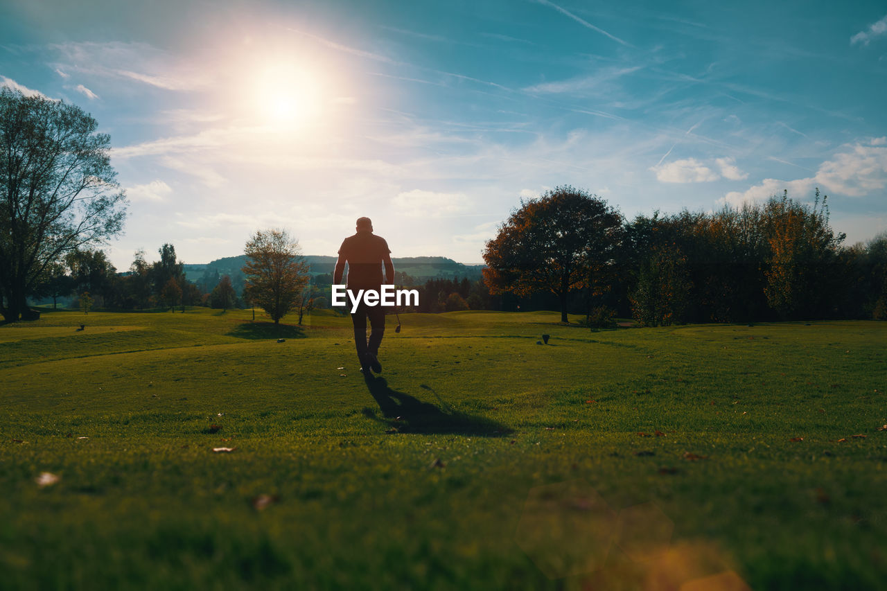 Rear view of man walking on golf course against sky