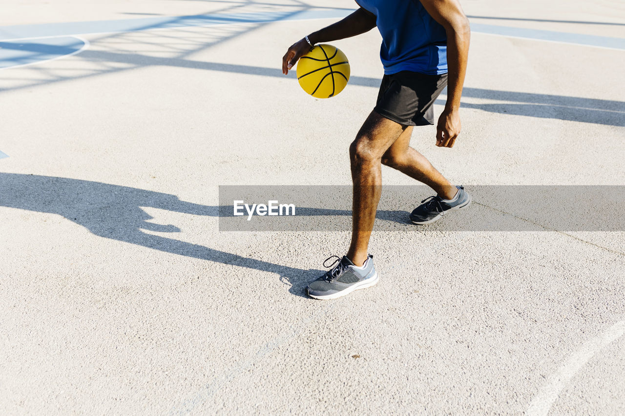 Young man dribbling basketball at sports court during sunny day
