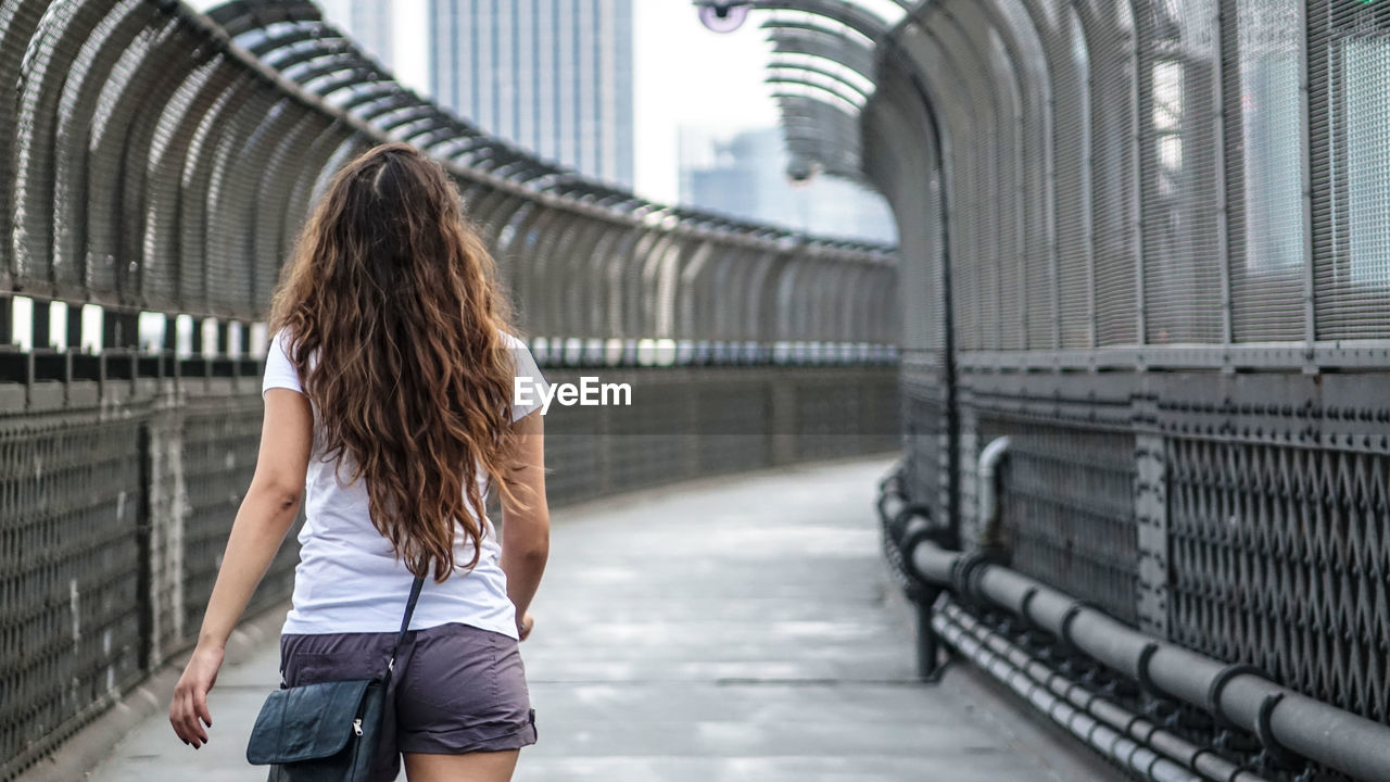 Rear view of woman walking on footbridge in city