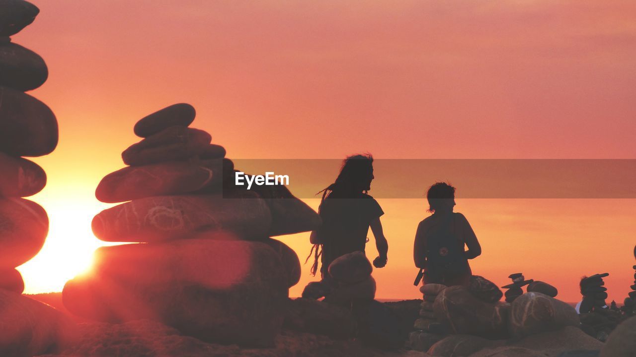 PEOPLE SITTING ON MOUNTAIN AGAINST ORANGE SKY