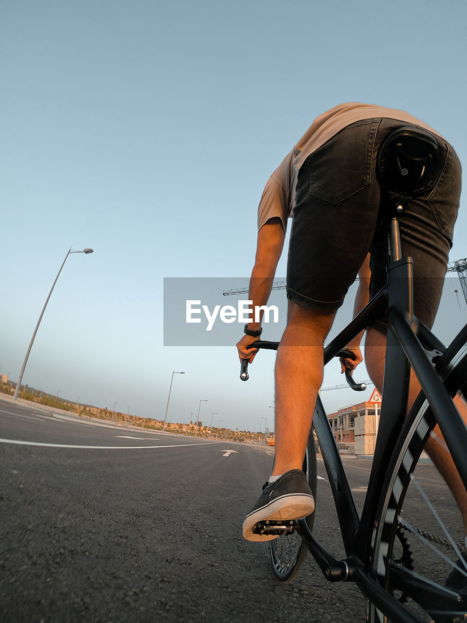 REAR VIEW OF MAN RIDING BICYCLE ON ROAD AGAINST CLEAR SKY