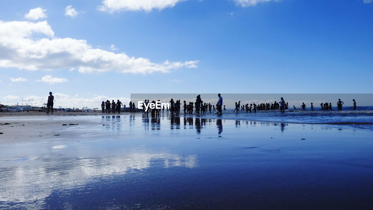 People on shore at beach against sky