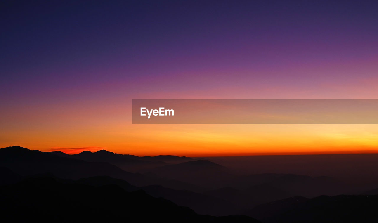 Scenic view of mountains against dramatic sky during sunset