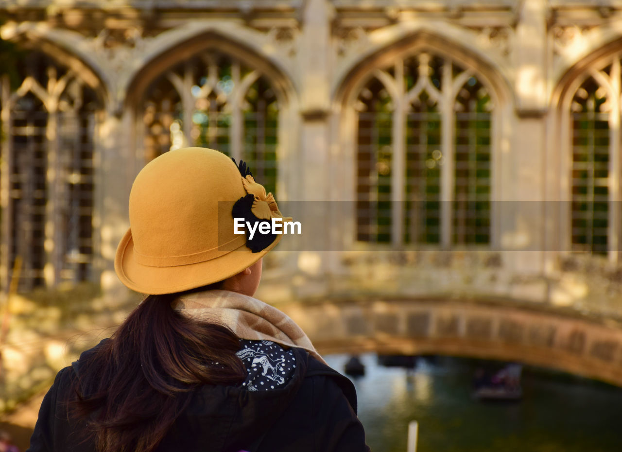 Rear view of woman in hat standing against building