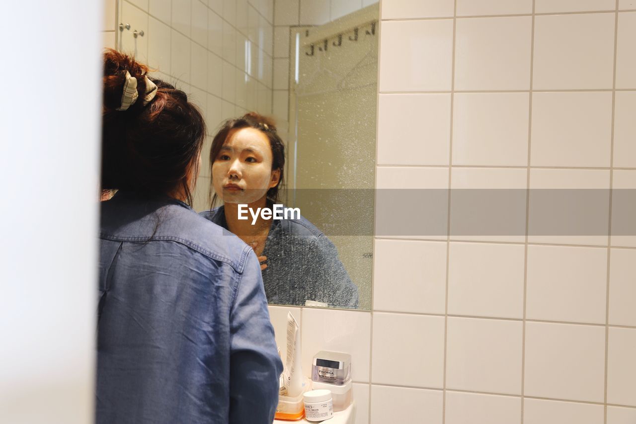 Young woman looking away while standing in bathroom