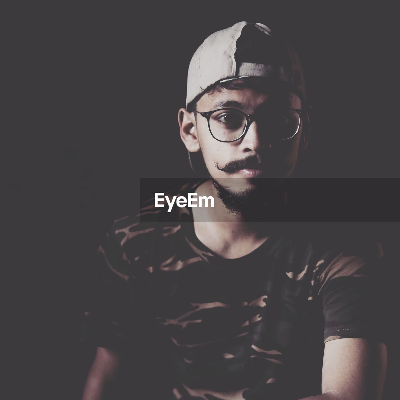 Portrait of young man wearing cap and eyeglasses in darkroom