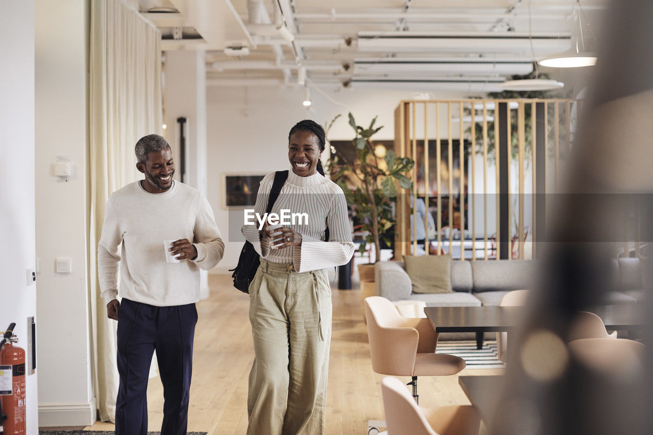 Happy male and female business professionals walking in office corridor