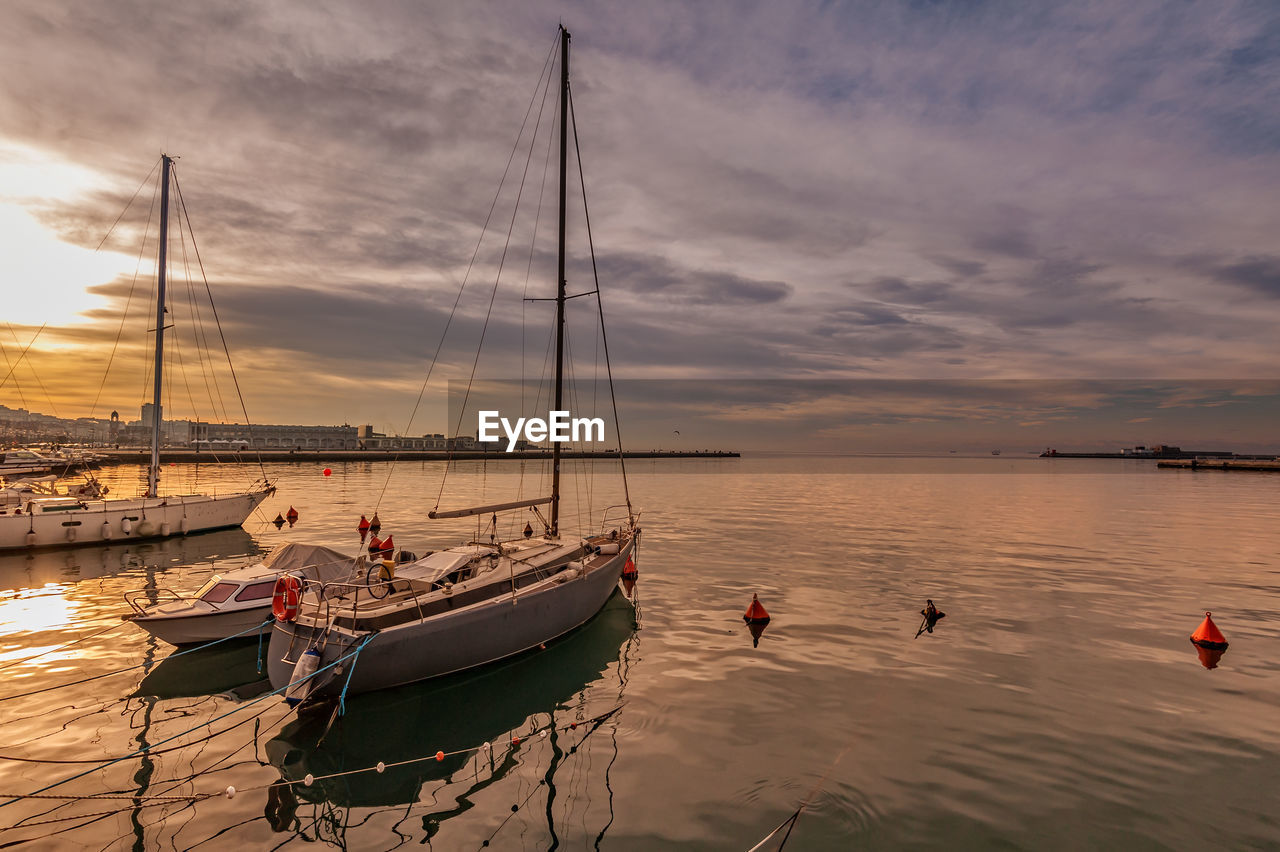 Sailboats moored in sea against sky during sunset