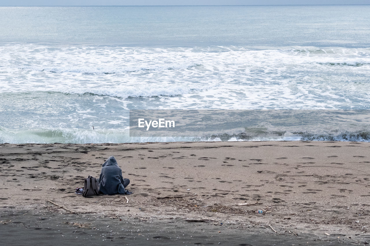 REAR VIEW OF WOMAN SITTING ON BEACH